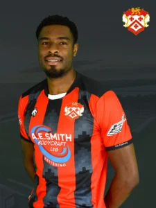 Male footballer in red-and-black striped kit posing for a team photo with Kettering Town FC crest on chest