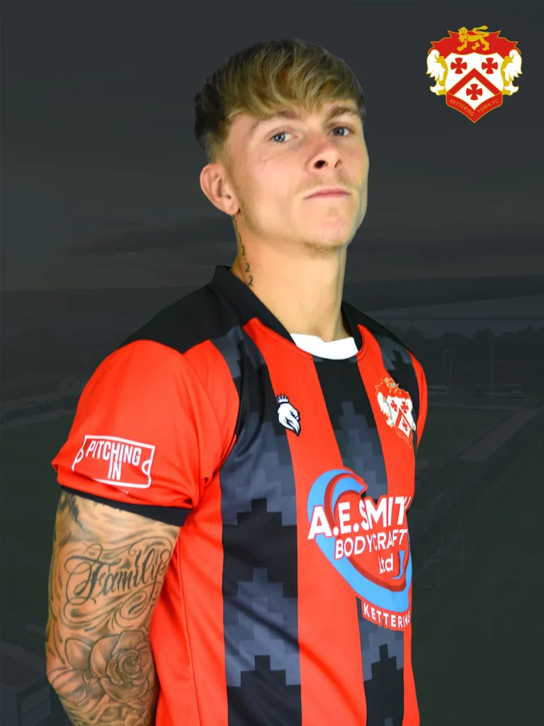 Portrait of a young man in a red and black striped football jersey, with team crest, tattoos on his forearm, against a dark background.