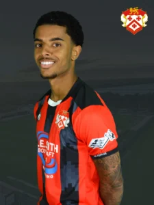 Smiling man in a red and black striped football jersey with a crest on the chest, posed against a dark background.