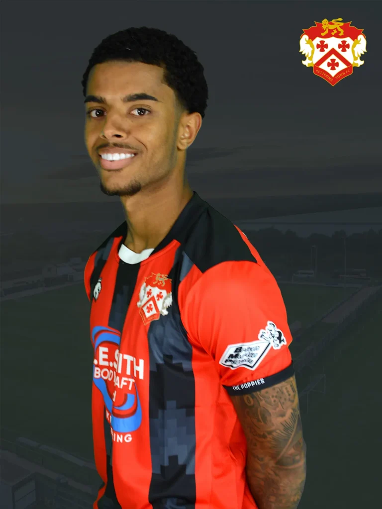 Smiling man in a red and black striped football jersey with a crest on the chest, posed against a dark background.