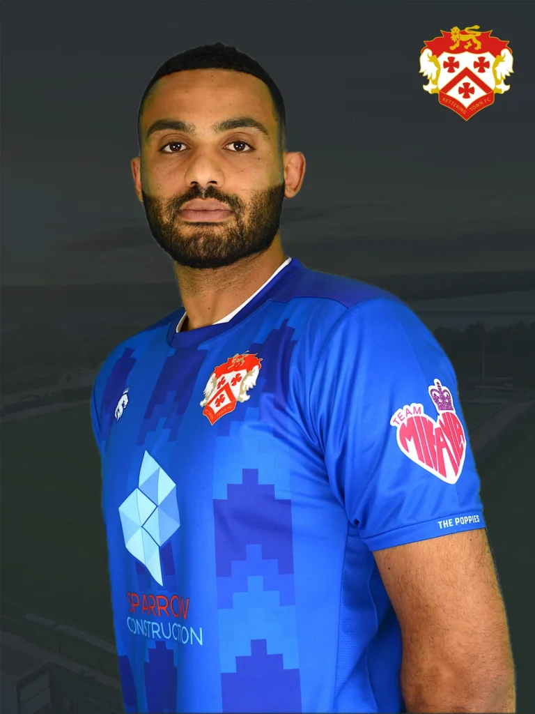 Male soccer player in a blue kit with club crest on chest against a dark background.