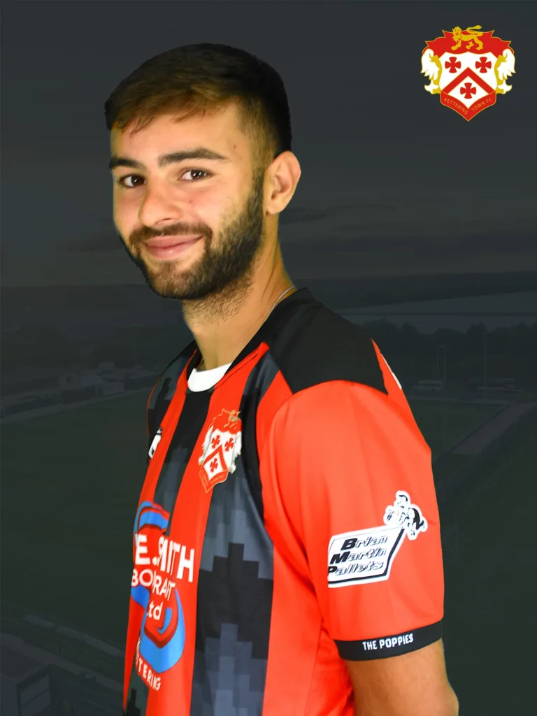 Portrait of a smiling man in a red and black football jersey, with a club crest visible in the top-right corner against a dark background
