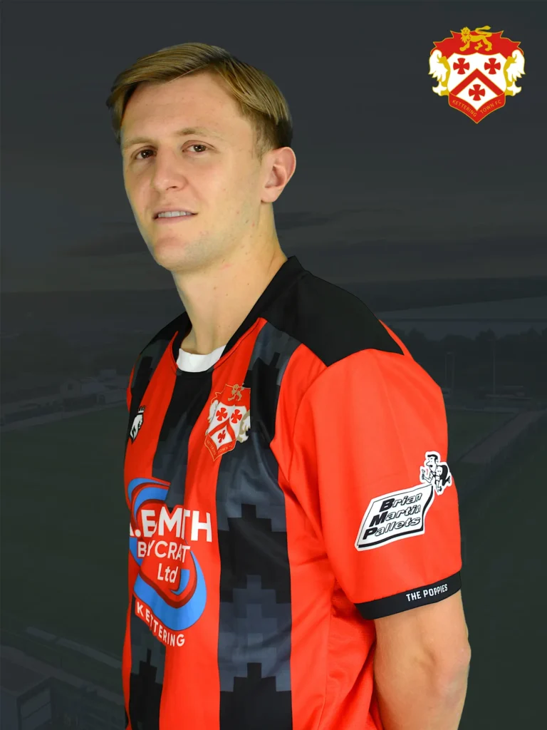 Portrait of a man in a red and black striped soccer jersey, with a club crest on the chest, against a dark background.